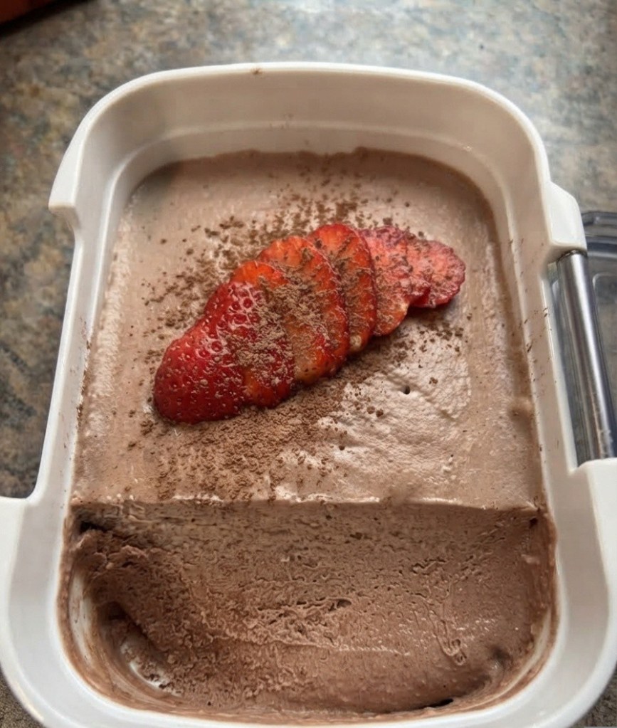 A container of chocolate ice cream topped with sliced strawberries and cocoa powder.