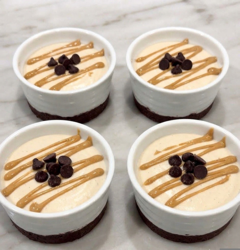 Four dessert cups with creamy filling topped with drizzled peanut butter and chocolate chips on a marble surface.