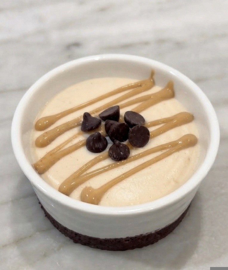 Creamy dessert in a white bowl with a chocolate crust, topped with chocolate chips and drizzled with peanut butter.
