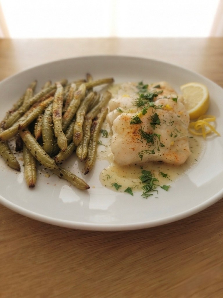 A plate featuring baked fish garnished with herbs and lemon, served alongside roasted green beans.