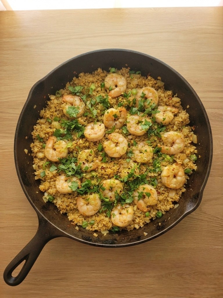 A cast iron skillet filled with shrimp and seasoned rice, garnished with fresh herbs.