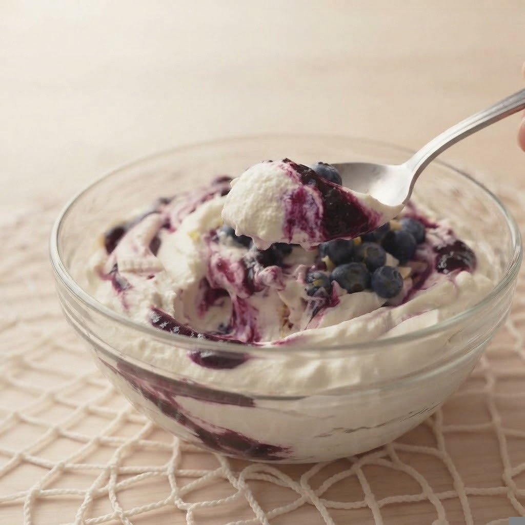 A bowl of creamy yogurt swirled with blueberry sauce and topped with fresh blueberries, with a spoon hovering above.